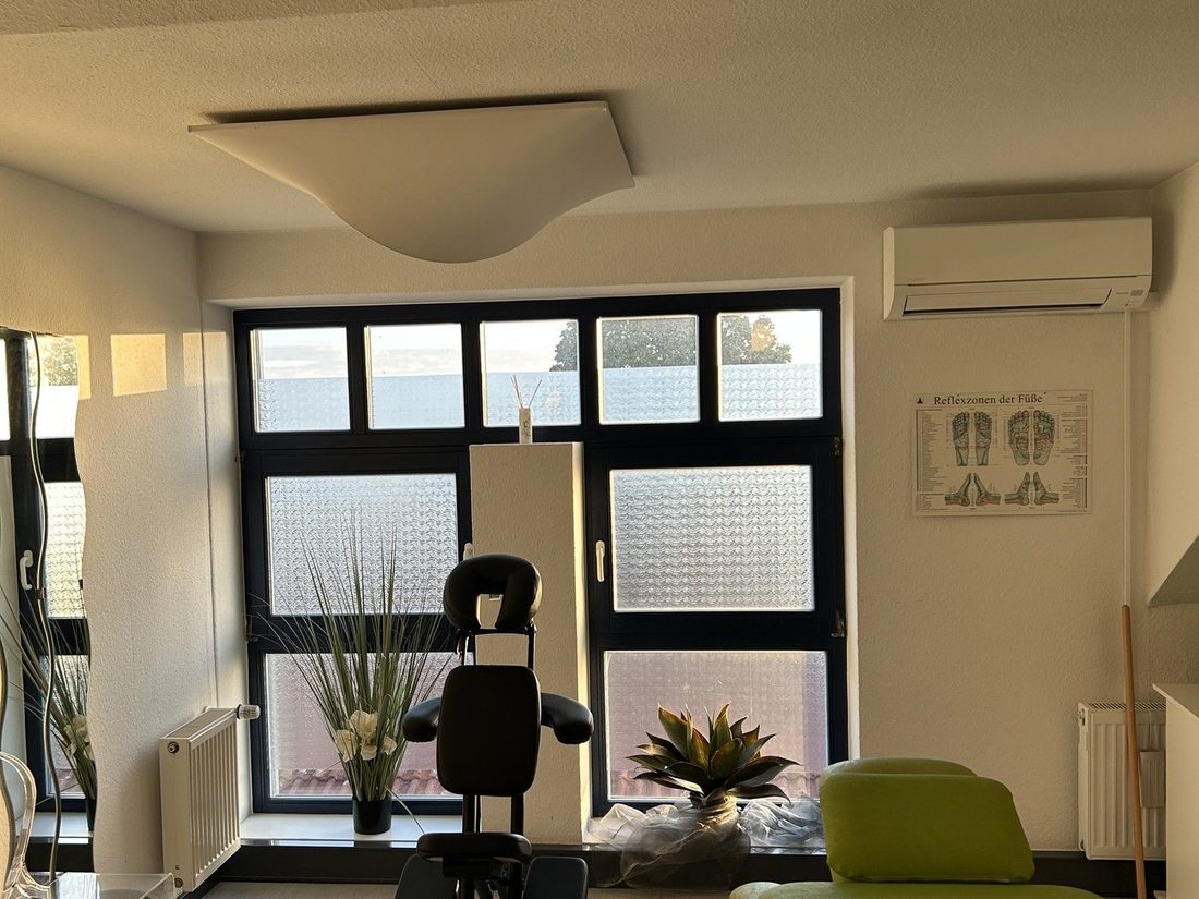Behandlungsraum mit Therapieliege und Trainingsgerät vor der Fensterfront